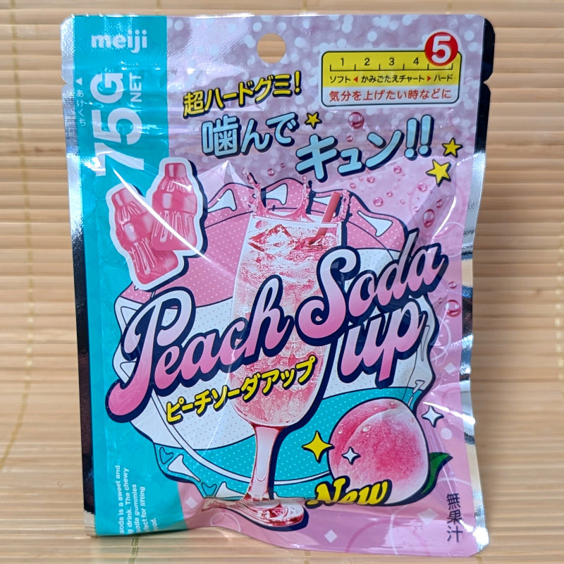 A 75 gram pack of Meiji Peach Soda Up Hard Gummy candies. A colorful pink and baby blue design. Displayed on a tatami background.