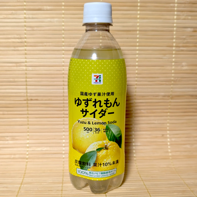 A bright yellow 500ml bottle of 7-Eleven Premium Yuzu & Lemon Soda showing yuzu fruit illustrations on a bamboo mat background.