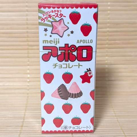A white and red 46g box of Meiji Apollo Strawberry Milk chocolates displaying cone-shaped chocolates and lucky star graphics on a bamboo mat background.