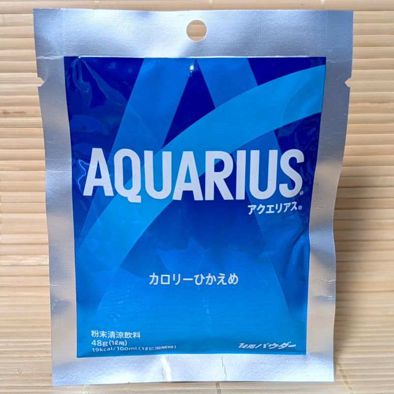 A blue and silver packet of Aquarius Sports Drink powder mix on a tatami background.