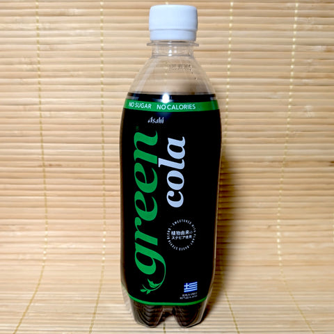 A sleek black and green 500ml bottle of Asahi Green Cola showing plant-derived stevia details and the Greek flag on a bamboo mat background.