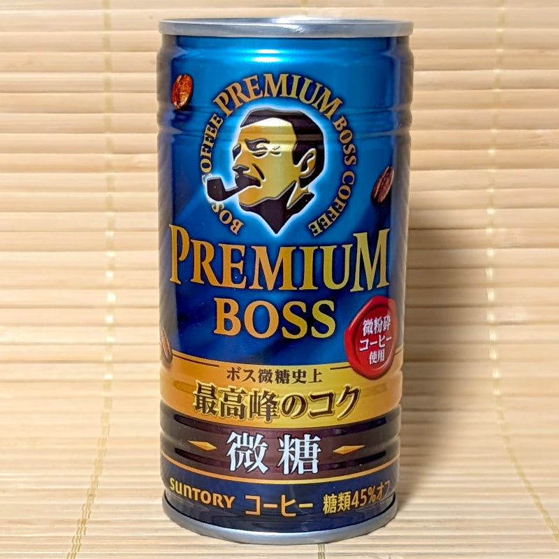 A deep blue 185g steel can of Suntory Premium BOSS Bitou Reduced Sugar Coffee showing the iconic pipe-smoking BOSS logo on a bamboo background.