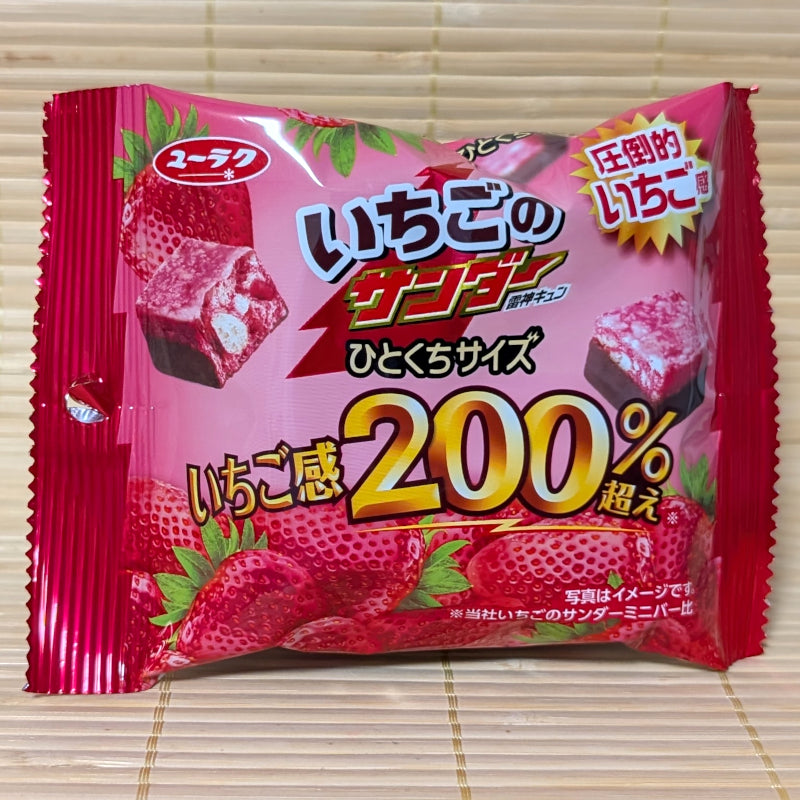 A pink foil pouch of Black Thunder Ichigo no Thunder on a tatami background featuring a cross-section of the 200% strawberry chocolate bit.