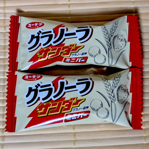 Two cream-colored wrappers of Black Thunder Granola mini bars featuring illustrations of strawberries and wheat stalks.