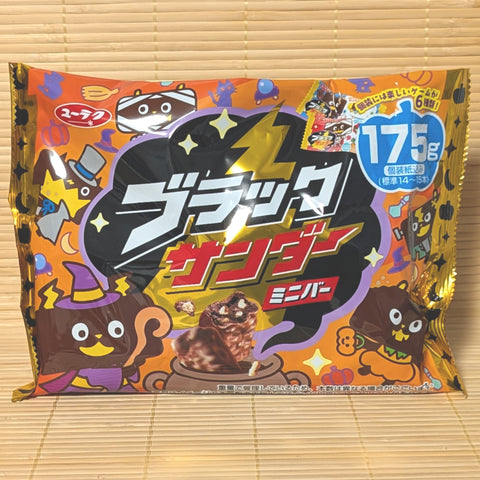 An orange and black 175g Halloween party bag of Black Thunder Minis showing costumed chocolate characters on a bamboo mat background.