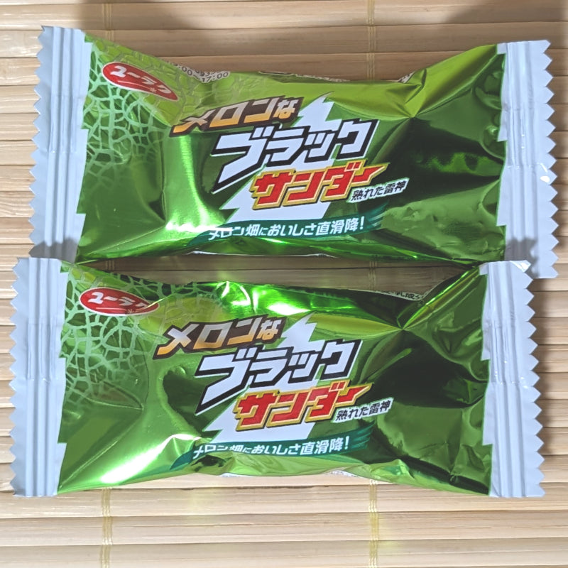 Two green metallic wrappers of Hokkaido Melon Black Thunder on a tatami background showing the melon graphic and lightning bolt logo.