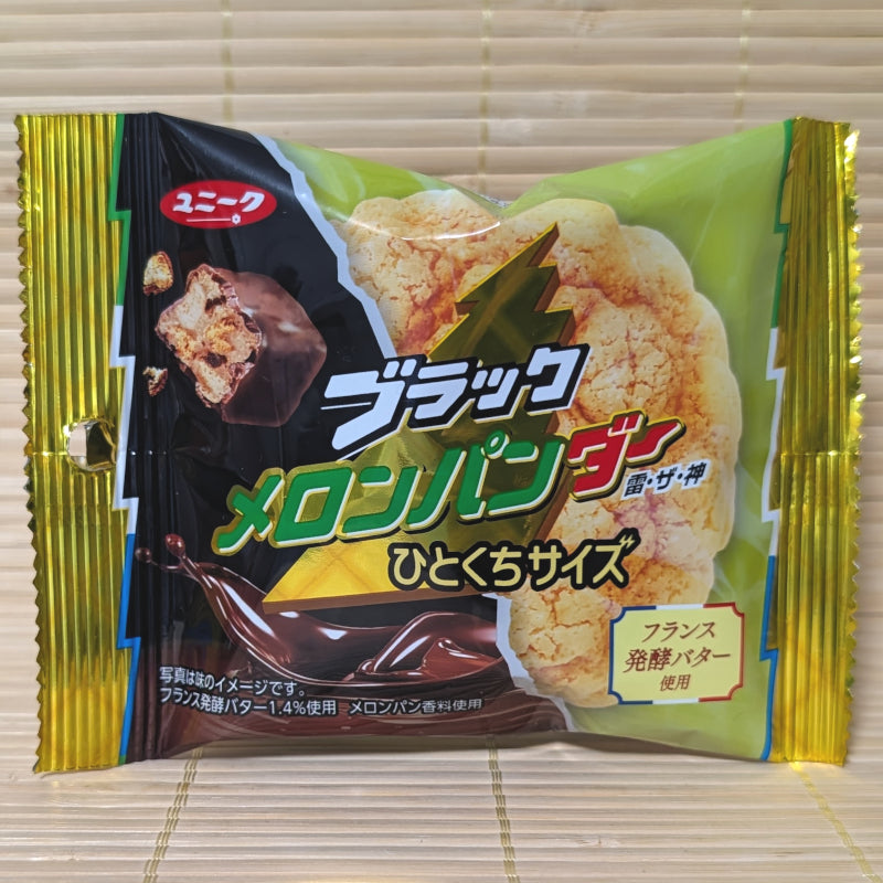 A green and gold foil bag of Black Thunder Melon Pan chocolate cubes featuring a picture of melon bread and splashing chocolate. Displayed on a tatami background.