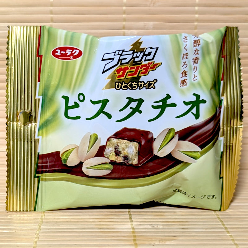 A light green and gold 44g pouch of Black Thunder Bites Pistachio chocolate showing whole pistachios and a cross section of a chocolate bite on a tatami mat background.