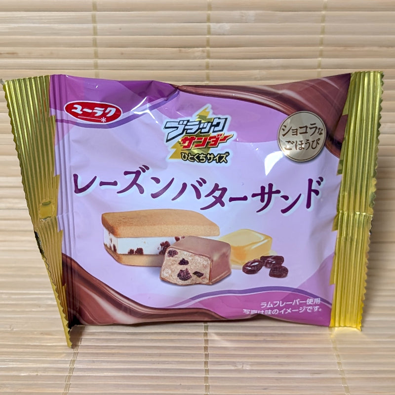 A light purple and gold 47g pouch of Black Thunder Raisin Butter Sandwich Chocolate showing butter sandwich graphics and raisins on a bamboo background.   
