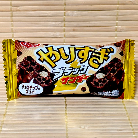 A gold and black 24g wrapper of Yuraku Yarisugi Black Thunder Chocolate Bar showing rich chocolate chip graphics on a bamboo background.   