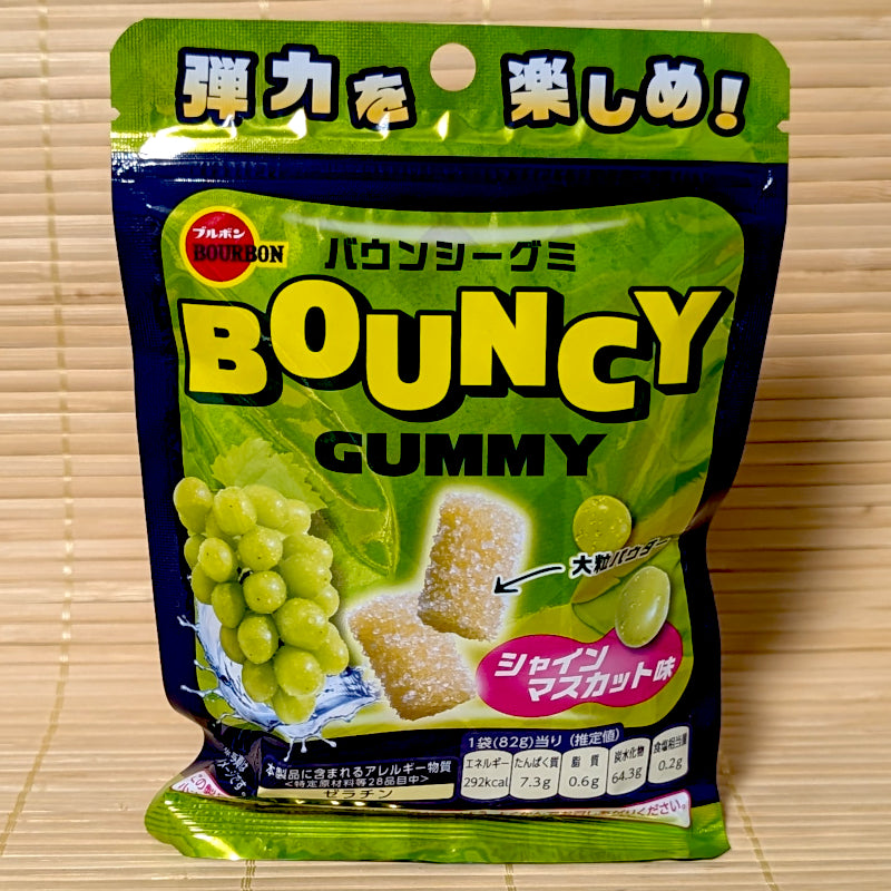 A bright green and blue pouch of Bourbon Bouncy Gummy Shine Muscat surrounded by green Shine Muscat grapes on a bamboo background.