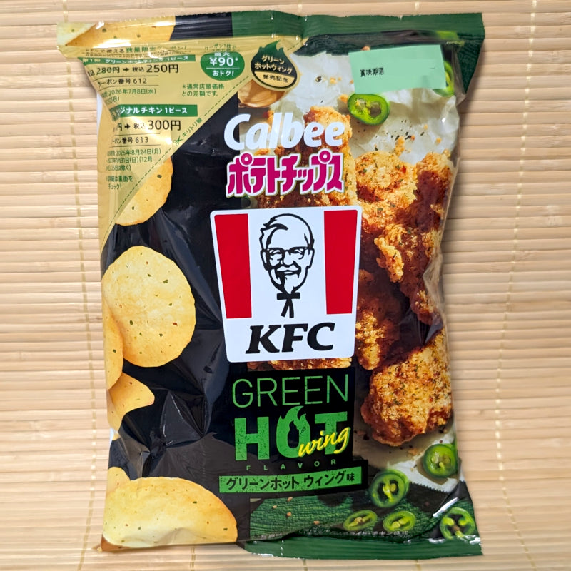 A black and deep green 62g bag of Calbee KFC Green Hot Wing chips showing the classic Colonel Sanders logo and green chili slices on a tatami background.