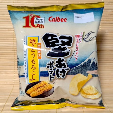 A 60g bag of Calbee Kata-Age Potato Chips featuring Hokusai-style Mount Fuji artwork, charred cobs of corn, and kettle chips on a bamboo mat background.
