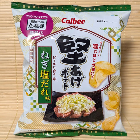 A cream and green 60g bag of Calbee Kata-Age Negi Shio Dare potato chips showing fan club logos and a plate of seasoned grilled meat on a tatami background.
