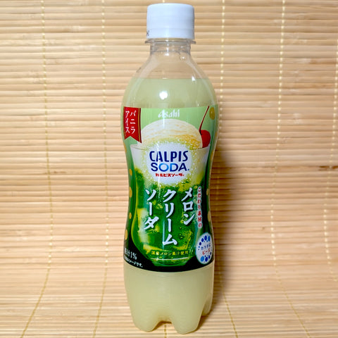 A 500ml PET bottle of light green Asahi Calpis Melon Cream Soda featuring a melon soda float graphic on a bamboo mat background.
