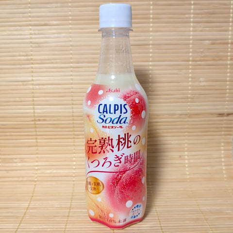 A 450ml PET bottle of Asahi Calpis Soda Ripe Peach displaying pink and yellow peach graphics on a bamboo mat background.
