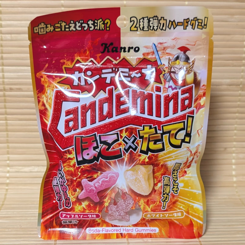 A colorful 60g pouch of Kanro Candemina Hoko x Tate gummies featuring fiery artwork, warrior graphics, and gummy pieces on a bamboo mat.