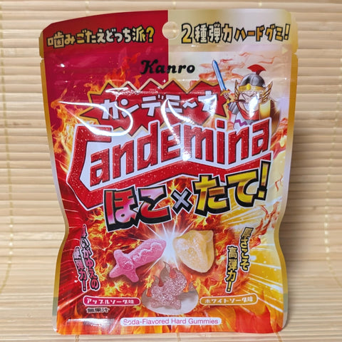 A colorful 60g pouch of Kanro Candemina Hoko x Tate gummies featuring fiery artwork, warrior graphics, and gummy pieces on a bamboo mat.