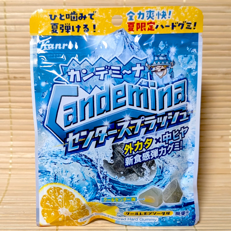 A icy blue and yellow 60g bag of Kanro Candemina Center Splash Cool Lemon Soda gummies showing waves, lemon slices, and a cross-section of a cooling center gummy on a bamboo mat background.