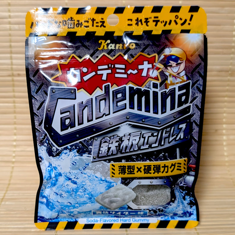 A black and yellow hazard-striped resealable pouch of Kanro Candemina Iron Plate Endless Soda gummy showing a grey steel tread plate shaped candy on a tatami background.