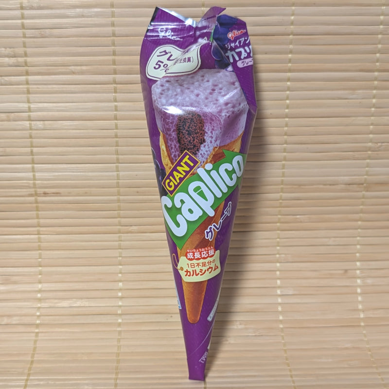 A vibrant purple foil-wrapped Glico Giant Caplico Grape chocolate cone on a natural bamboo mat background.
