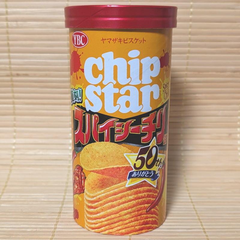 An orange and red canister of YBC Chip Star Spicy Chili chips with a 50th-anniversary logo, photographed on a traditional Japanese tatami background.