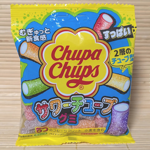A bright yellow and blue bag of Chupa Chups Sour Tube gummies showing colorful 2-layer tube shapes in various fruit flavors. Displayed on a tatami background.