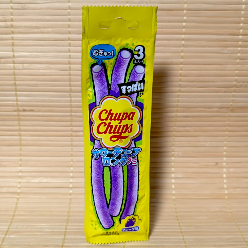 A tall yellow pack featuring three long purple sour tube gummies with a white filling and a grape illustration. Displayed on a tatami background.