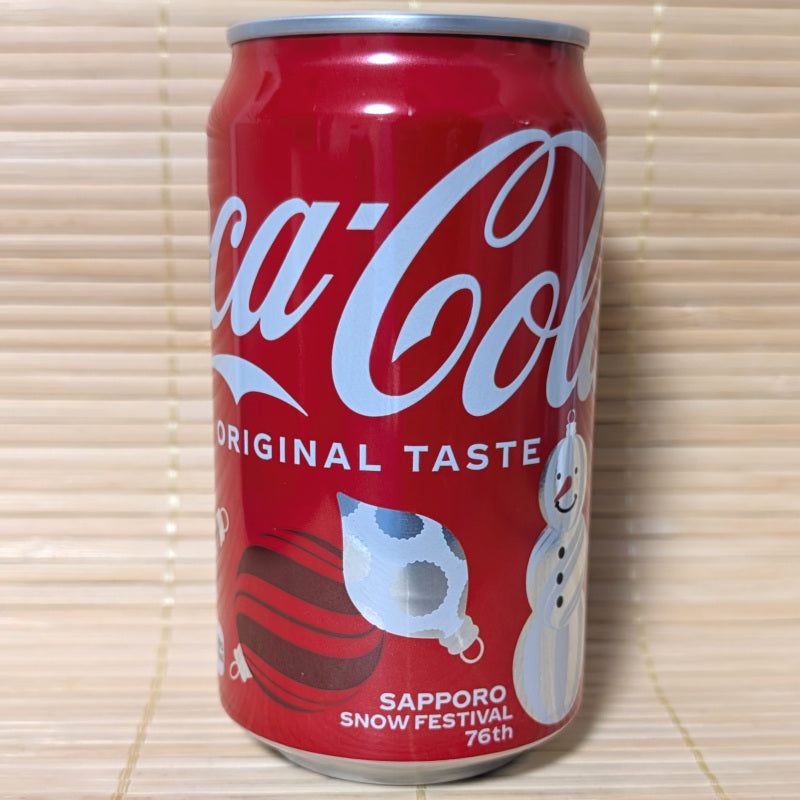 A 2026 Coca-Cola Sapporo Snow Festival can with a snowman and tree decoration designs. Displayed on a tatami surface.
