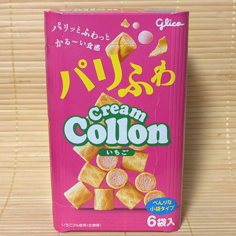 A bright pink large 81g box of Glico Cream Collon Strawberry containing 6 mini packs with waffle roll artwork on a bamboo mat background.