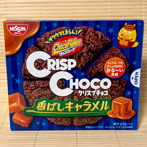 A bright blue slide-out box of Crisp Choco Aromatic Toasted Caramel showing a chocolate cornflake wheel and caramel squares on a bamboo background.   