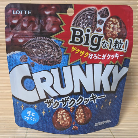 A blue and red stand-up pouch of Lotte Crunky BIG Choco COOKIE Balls showing graphics of a dark cream biscuit and cross-sections of the crunchy candy spheres, on a tatami background.
