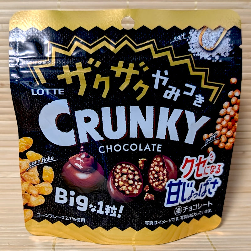 A black and gold stand-up pouch of Lotte Crunky BIG Extra Crispy Chocolate Balls featuring corn flake, salt, and cross-section candy graphics on a tatami background.
