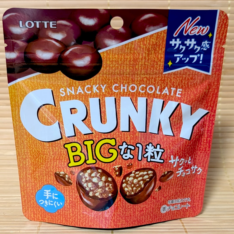 An orange and red stand-up pouch of Lotte Crunky BIG Chocolate Balls featuring cross-section graphics of crispy malt-filled chocolate spheres, on a tatami mat background.