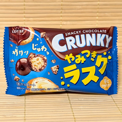 A bright blue 32g bag of Crunky Yamitsuki Rusk Chocolate Balls showing buttery rusk graphics and chocolate balls on a bamboo background.
