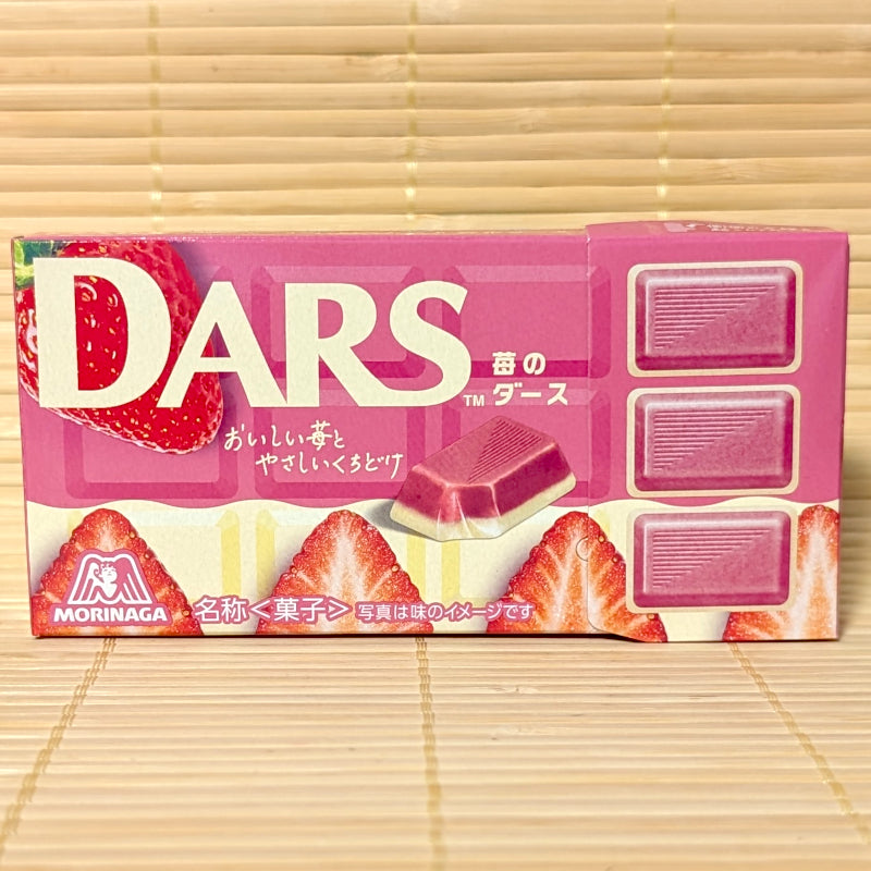 A bright pink 42g box of DARS Strawberry and White chocolates with fresh sliced strawberry graphics on a bamboo mat.