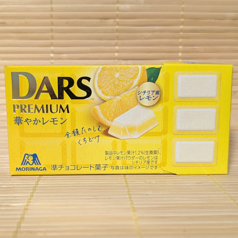 A bright yellow slide-out box of Morinaga DARS Premium Hanayaka Lemon chocolate showing fresh sliced lemons and three white chocolate blocks on a tatami background.