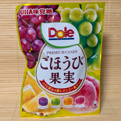 A yellow UHA Mikakuto bag on a tatami background with the Dole logo and images of grapes, muscat, pineapple, and peaches.