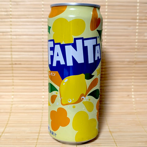 A yellow and orange 500ml tall can of Japanese Fanta Lemon soda featuring retro flower shapes and carbonation bubbles against a bamboo background.