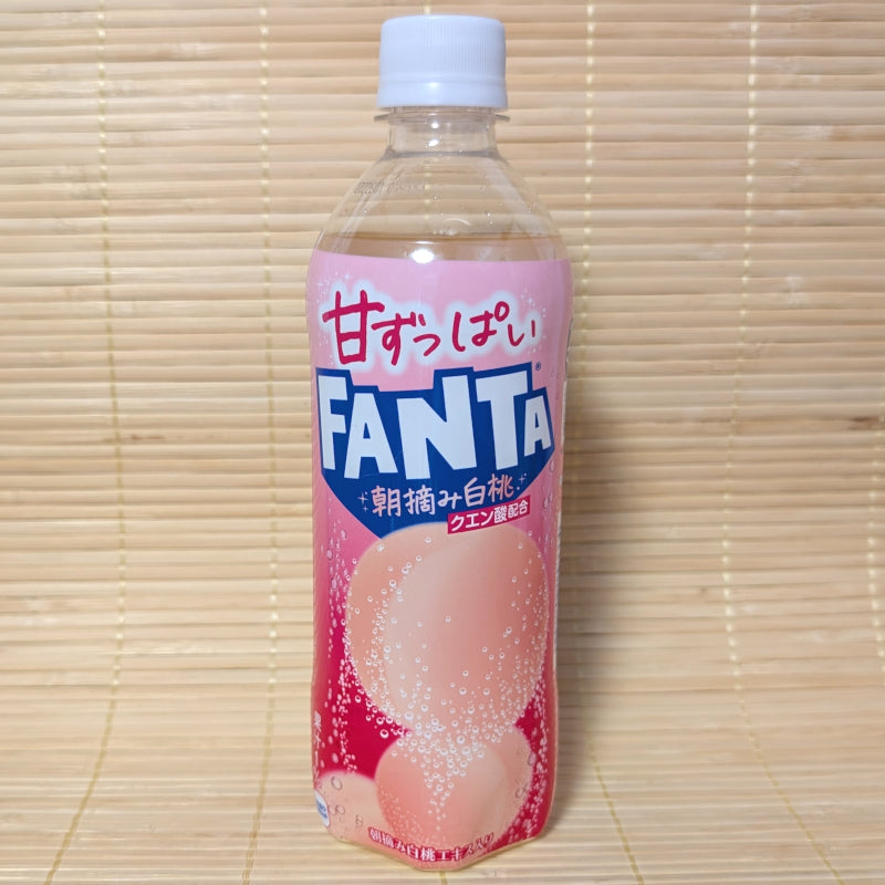 A 490ml bottle of Japanese Fanta White Peach soda with a pink label showing bubbly peaches, set against a traditional tatami background.