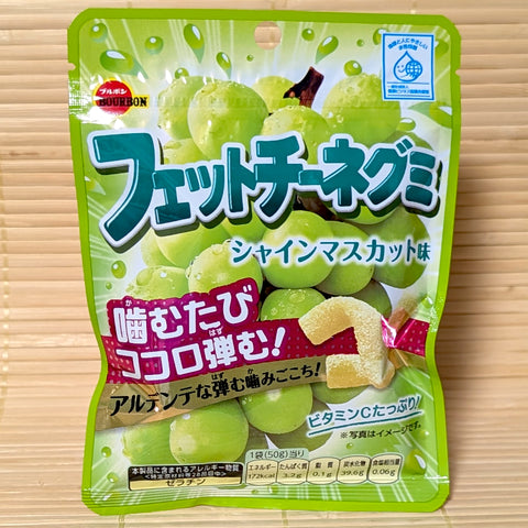 A green 50g pouch of Bourbon Fettuccine Gummy Shine Muscat showing grape graphics and sour ribbon gummies on a bamboo background.