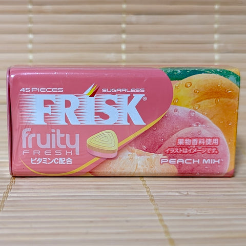 A pink and orange metal tin of Frisk Fruity Fresh Peach Mix mints featuring a triangular two-toned tablet and fresh peach illustrations. Displayed on a tatami background.