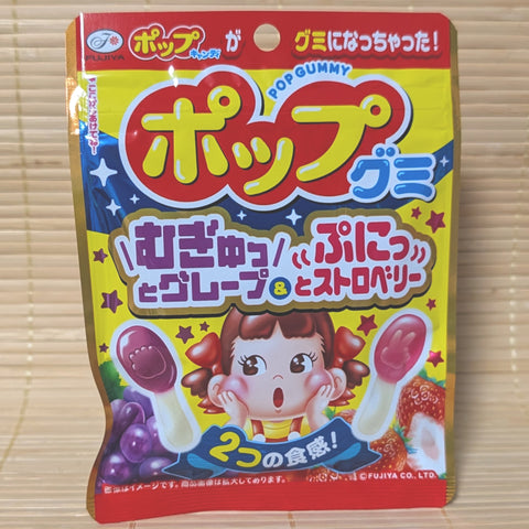 A bright yellow Fujiya POP Gummy bag on a tatami background featuring Peko-chan and lollipop-shaped grape and strawberry gummies.
