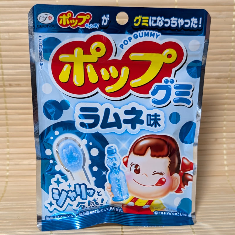 A blue and white resealable pouch of Fujiya POP Gummy on a tatami background featuring Peko-chan, a bottle of ramune, and various gummy shapes.