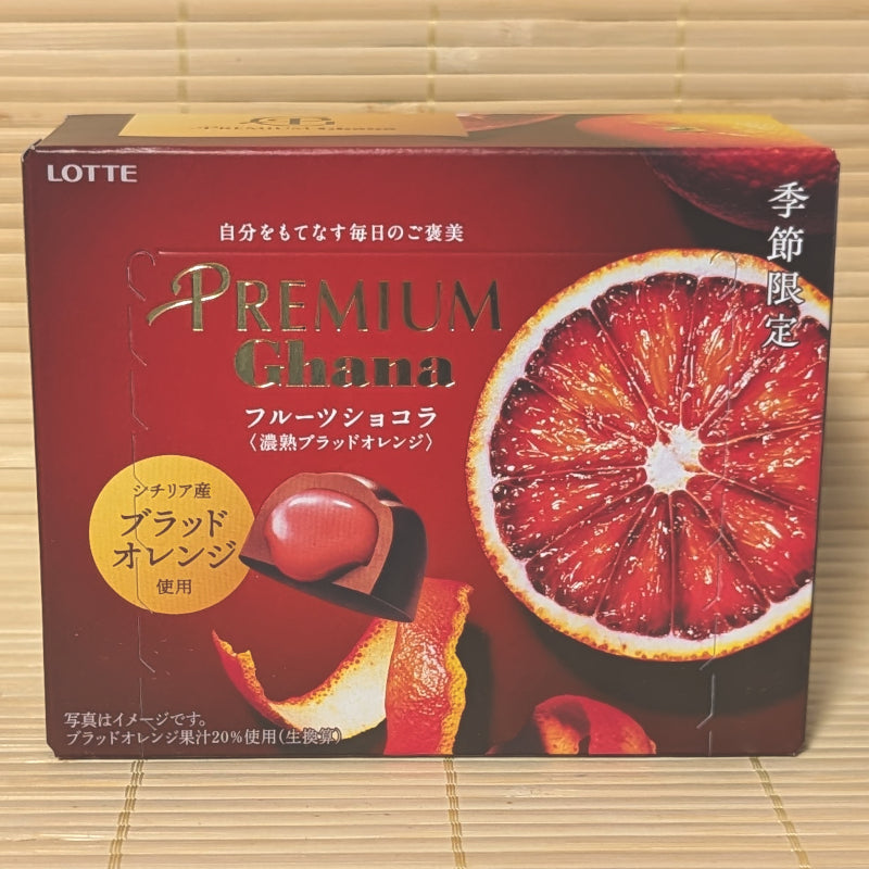 A deep red 65g box of Premium Ghana Fruit Chocolat Rich Blood Orange showing a sliced blood orange and filled chocolate piece on a bamboo background.   