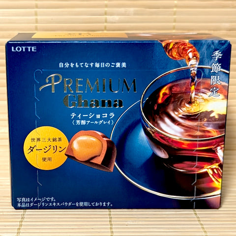 A dark blue 65g box of Premium Ghana Tea Chocolat Darjeeling Earl Grey showing a glass teacup and filled chocolate piece on a bamboo background.   