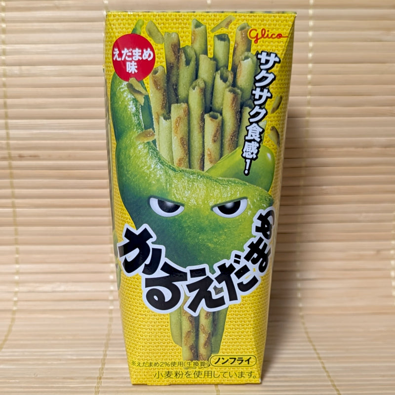 A yellow 36g box of Glico Karuedamame potato sticks featuring a green edamame pod character with eyes against a textured tatami background.