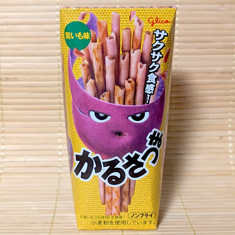 A yellow and purple 36g box of Glico Karusatsuma purple sweet potato sticks with character artwork on a bamboo mat background.