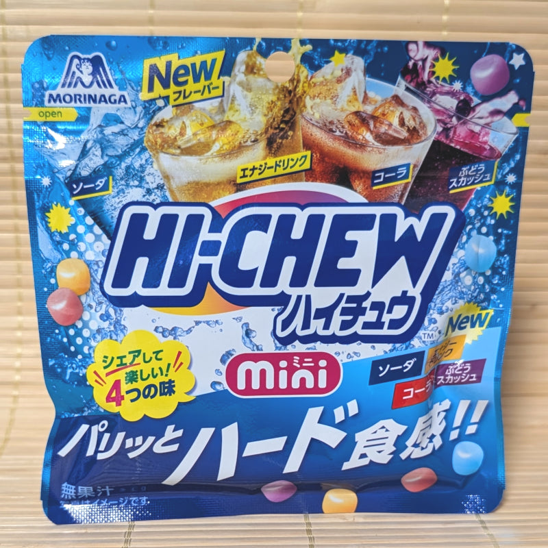 A bright blue resealable pouch of Hi-Chew Mini candies on a tatami background, featuring glasses of soda and energy drinks with small colorful candy beans.
