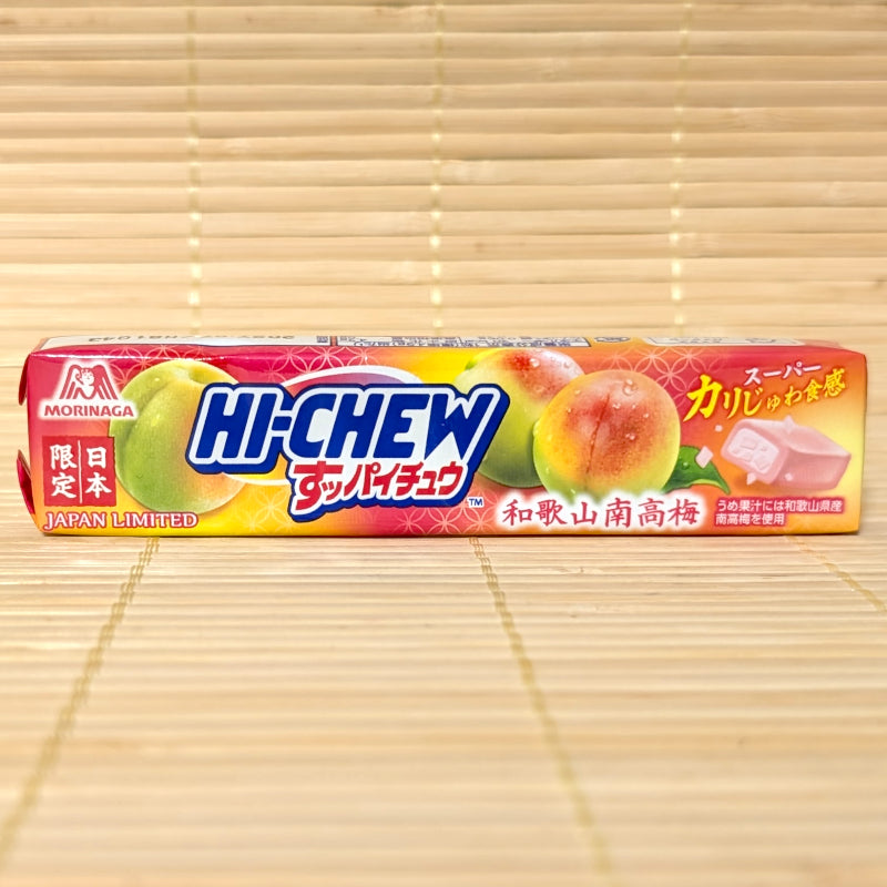 A bright pink stick pack of Morinaga Suppai Chew Wakayama Nanko Plum candy with plum illustrations on a bamboo mat background.